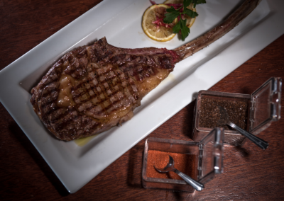 A plate with a Tomahawk steak, sliced lemon and spices on the side