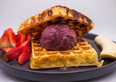 A plate of Waffles with icecream and strawberries and banana on the side