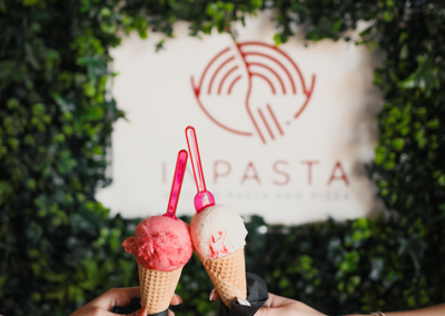 Two People showing the Ice cream cones they got at the Inpasta restaurant, with the logo behind them