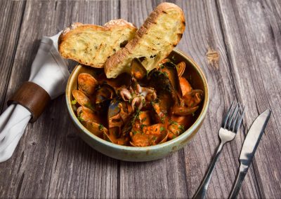 alt="a bowl filled with mussels and bread on top of a wooden table"